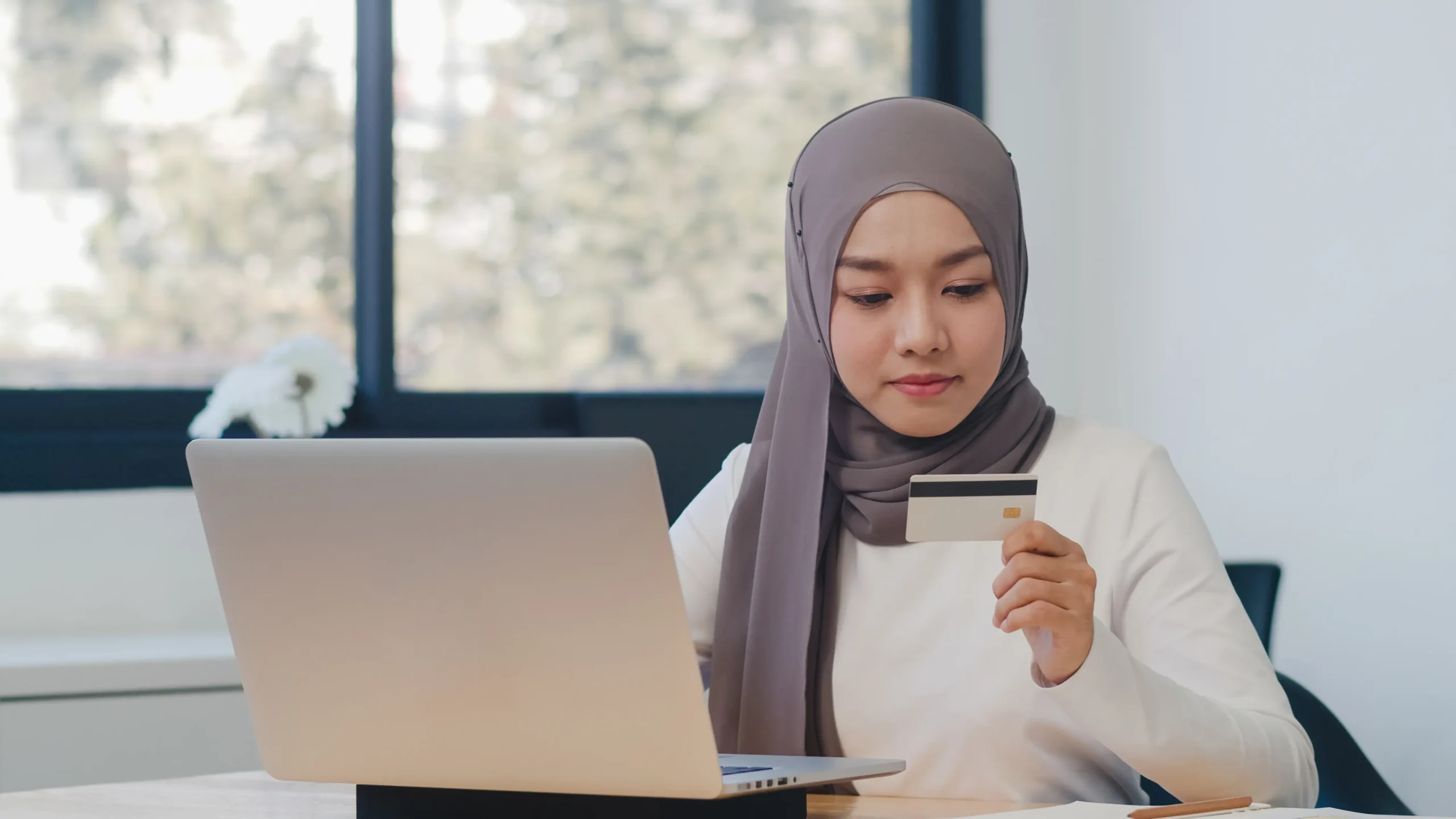 Muslim woman checking financial expenses using laptop and card, illustrating issues of unpaid spousal maintenance